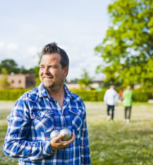Smiling man looking away while holding boule balls at park